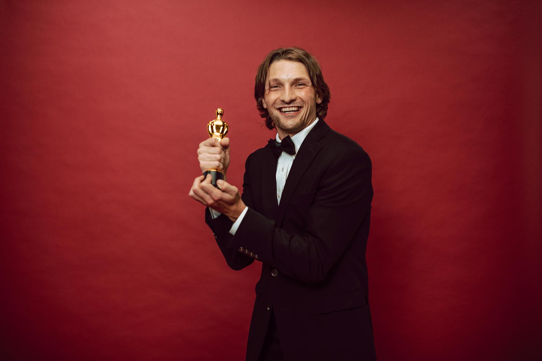 Um homem feliz vestindo um terno  preto e segurando seu troféu