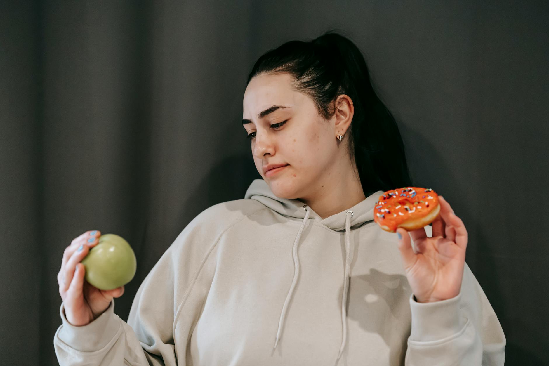 thoughtful woman choosing between green apple and donut